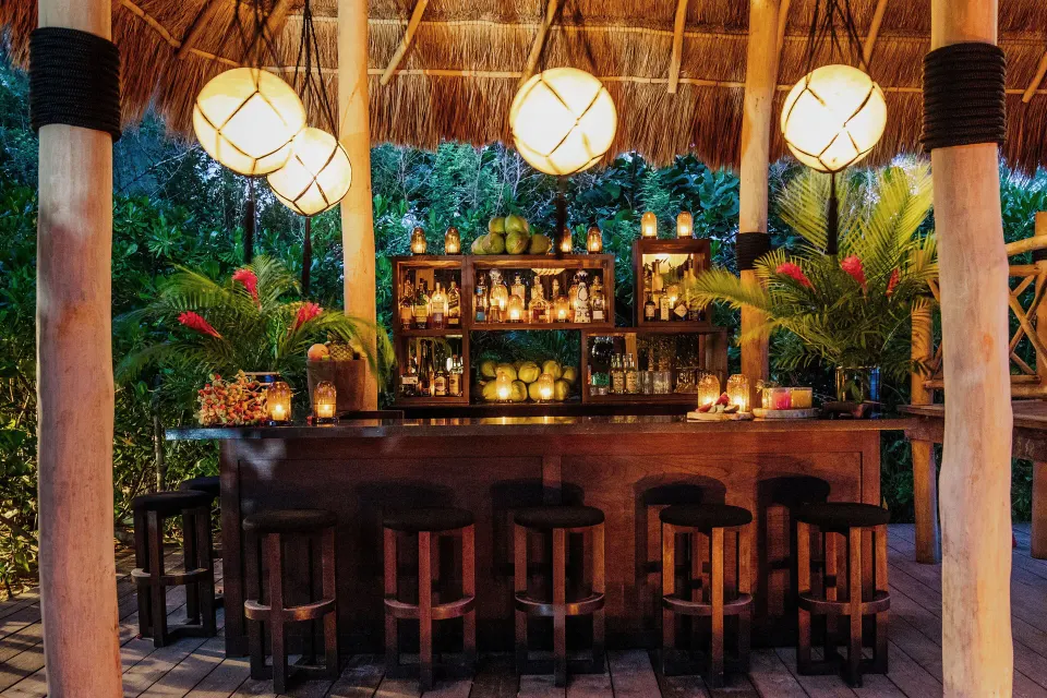 Thatched tropical bar lit by lanterns surrounded by foliage at Hotel Esencia.