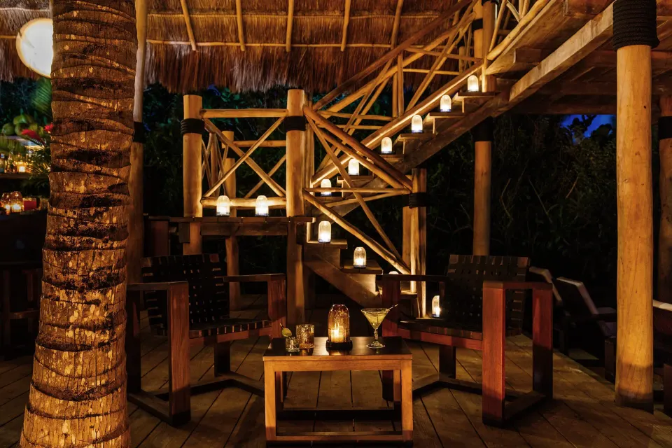 Candlelit wooden deck seating and staircase by palms at Hotel Esencia.