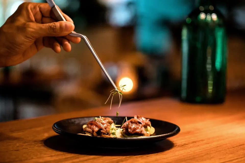 Chef adding garnish to plated bites on a wooden counter at Hotel Esencia