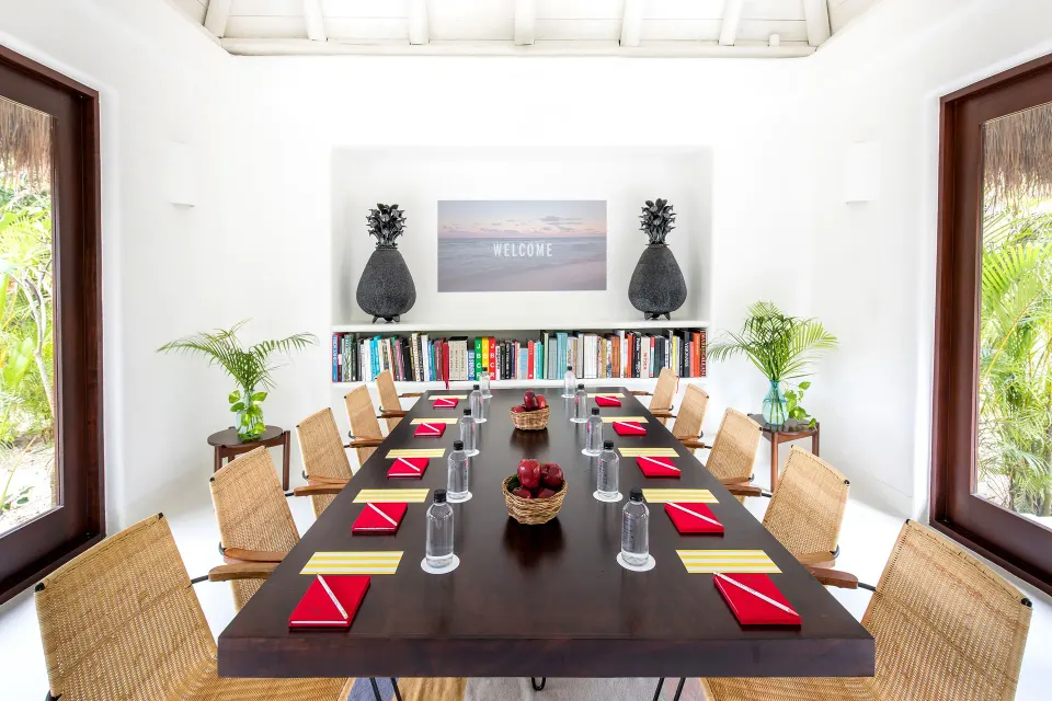 Meeting table set with red napkins and bookshelves inside a bright room at Hotel Esencia