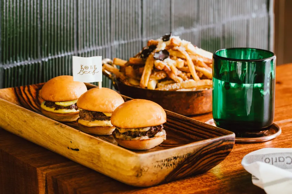 Wooden board with three mini burgers and a bowl of fries at Hotel Esencia.