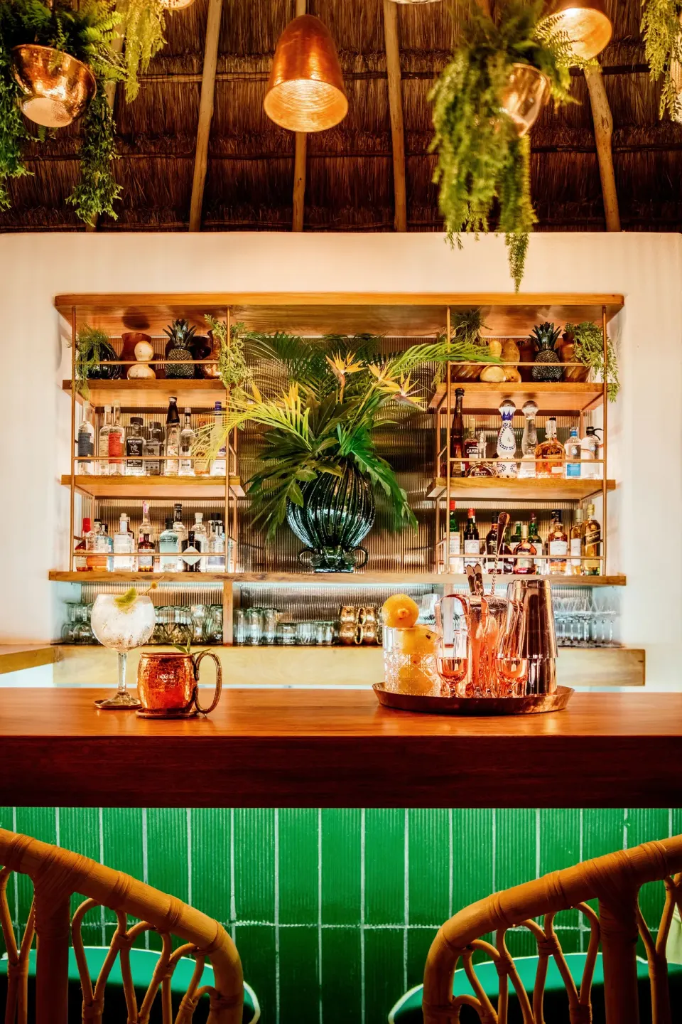 Backlit palapa bar with green-tiled counter and copper accents at Hotel Esencia