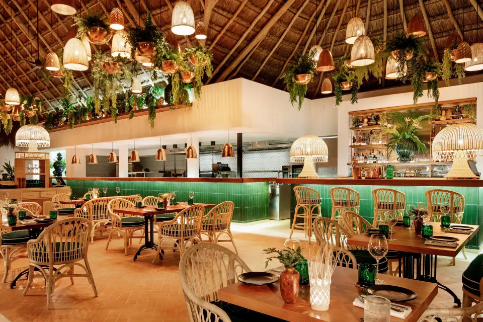 Thatched-roof dining room with rattan chairs and green-tiled bar at Hotel Esencia.
