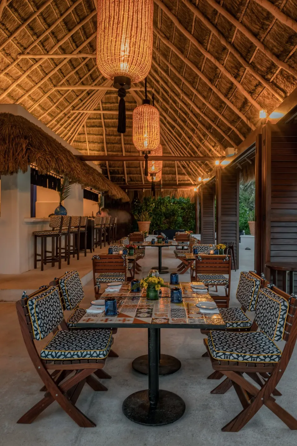 Long palapa dining table with patterned chairs and hanging lamps at Hotel Esencia.