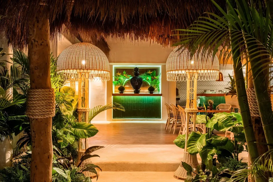 Tropical restaurant entry with woven lamps and green bar at Hotel Esencia