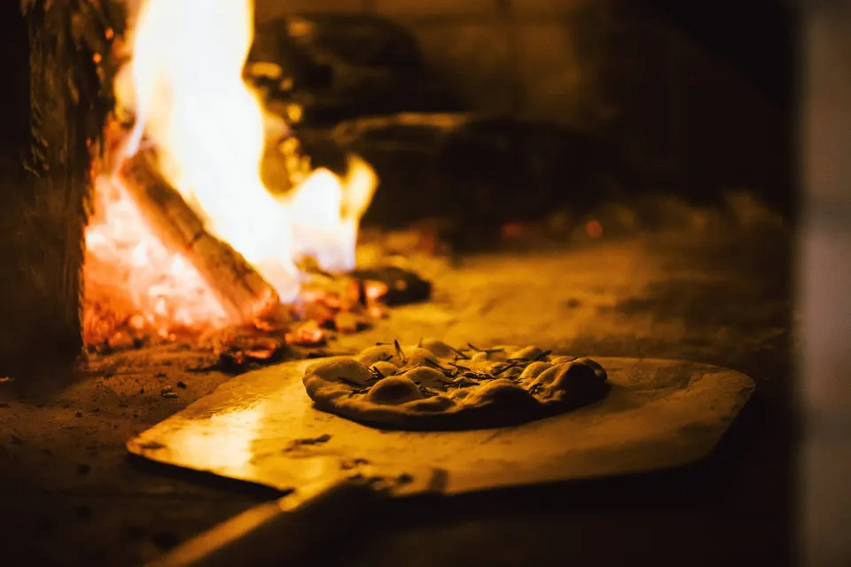Wood-fired pizza cooking on a peel inside a stone oven at Hotel Esencia.