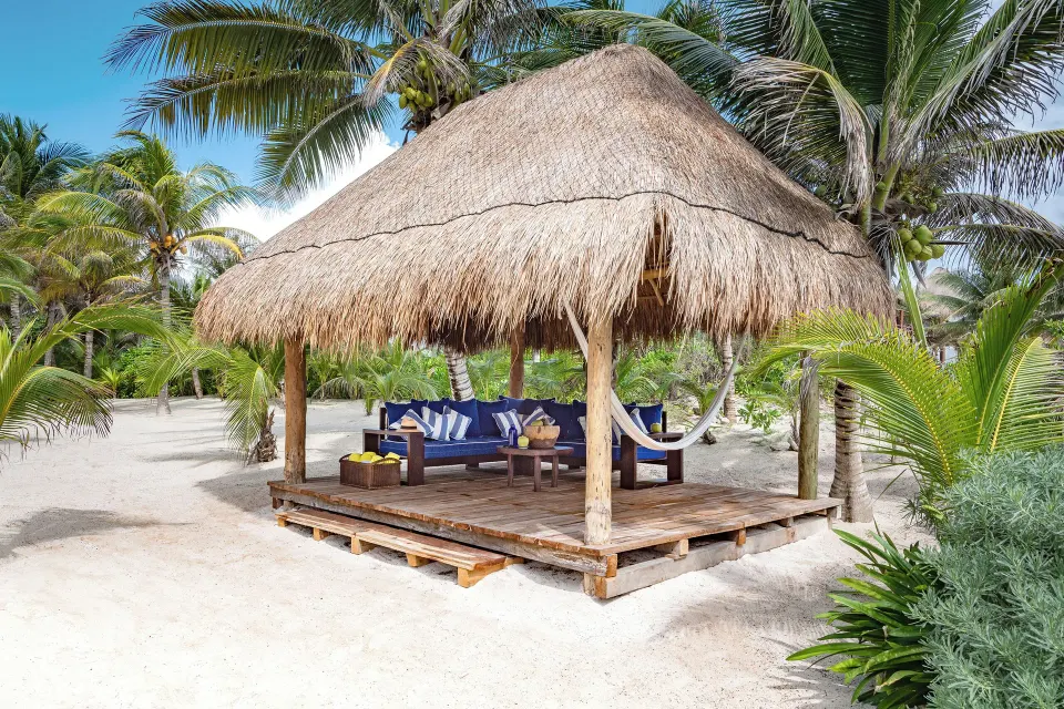 Standalone palapa cabana with cushioned seating and hammock on the sand at Hotel Esencia.