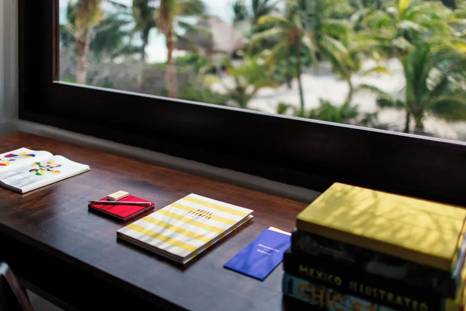 Desk with notebooks and books overlooking palms and the beach at Hotel Esencia.