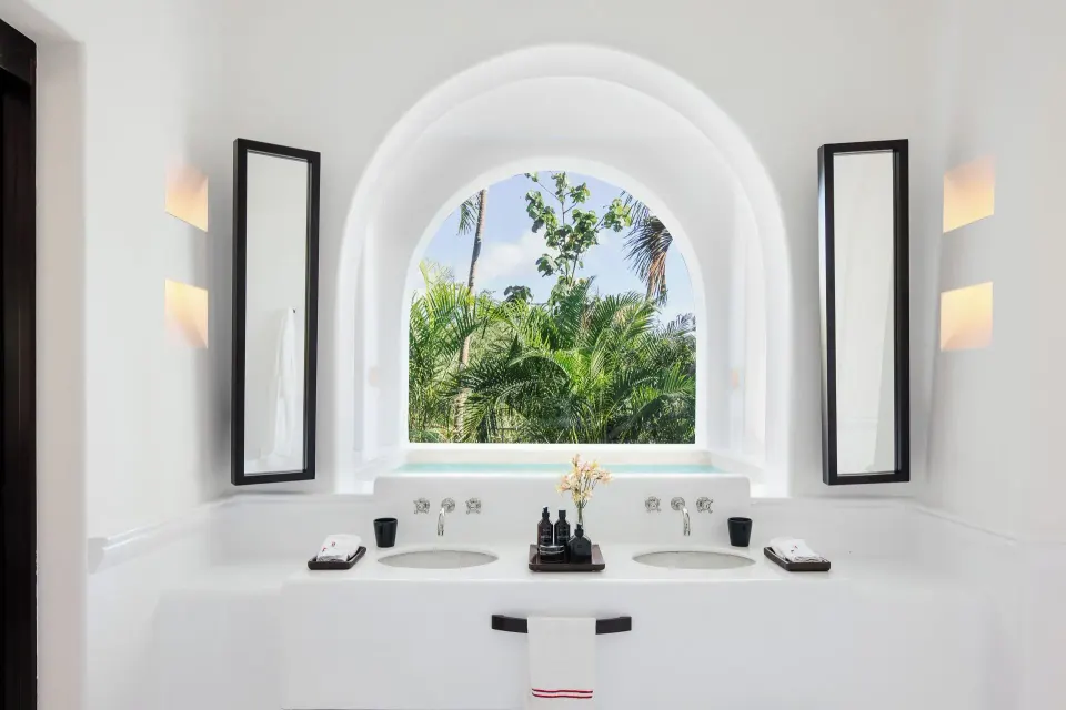 Twin basins beneath an arched window framing palm trees in the Jungle Suite at Hotel Esencia