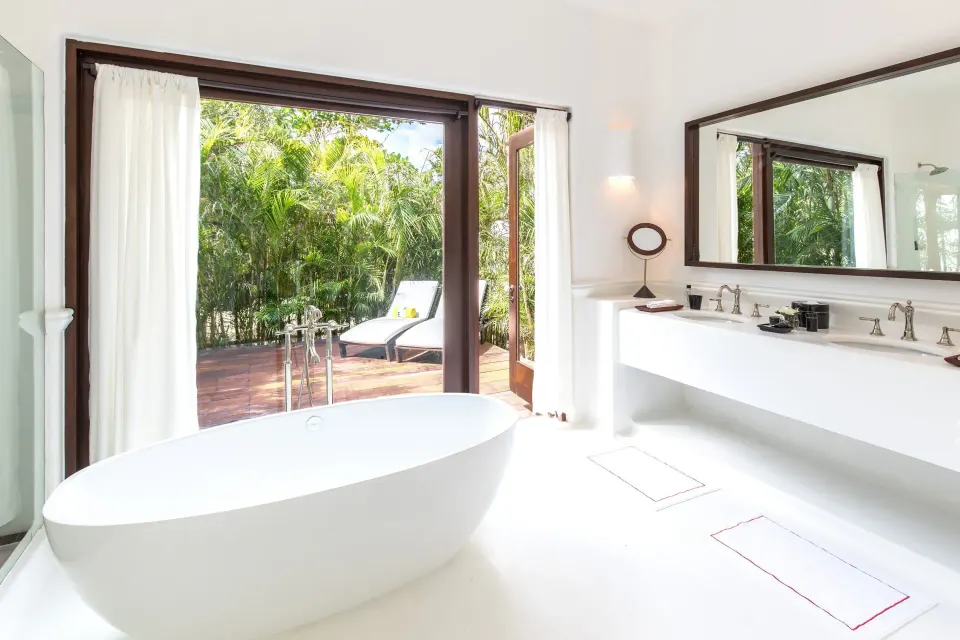 Freestanding tub and open doors to a wooden deck with loungers in a Jungle Suite at Hotel Esencia.