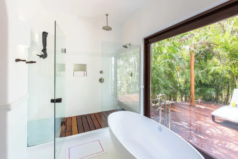 Bathroom with freestanding tub, glass-walled shower, and open doors to a tropical deck in a Jungle Suite at Hotel Esencia.