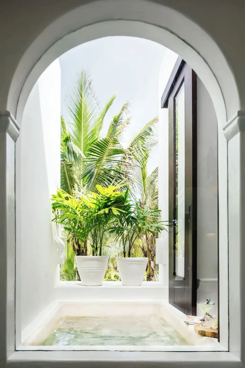 Arched window framing a private soaking tub and tropical plants at Hotel Esencia
