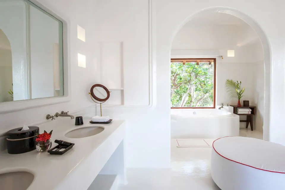 Bright white bathroom with arched doorway leading to garden-facing tub at Hotel Esencia