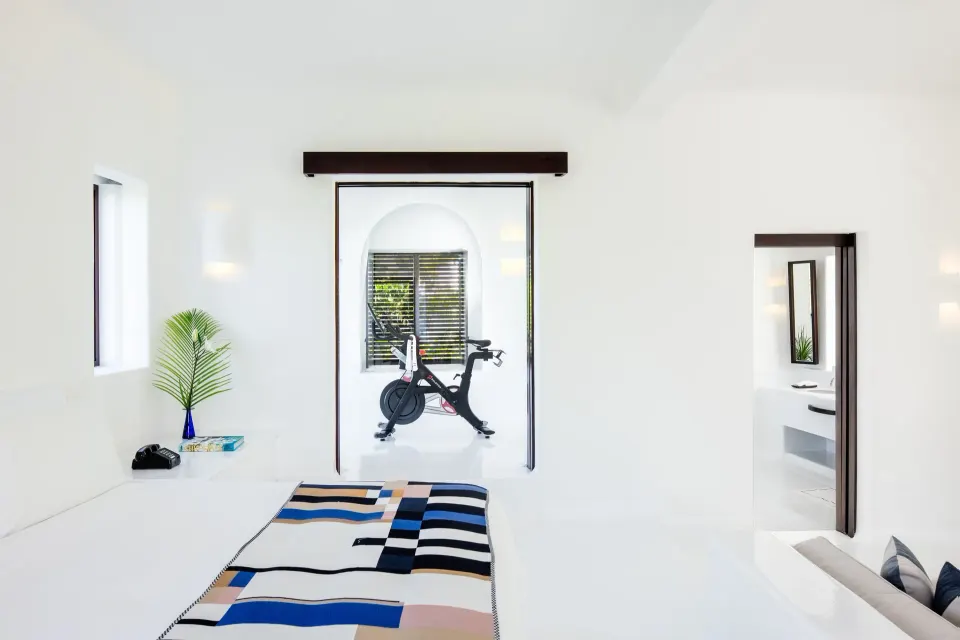 Minimal bedroom with exercise bike visible through doorway at Hotel Esencia