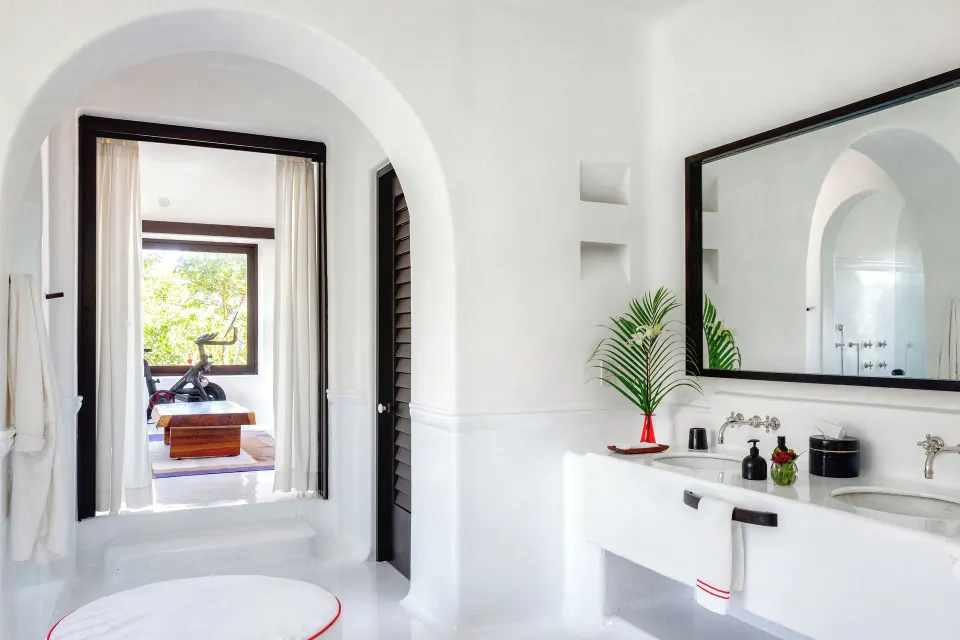 Bathroom with white sink, large mirror and arched doorway leading to lounge at Hotel Esencia.