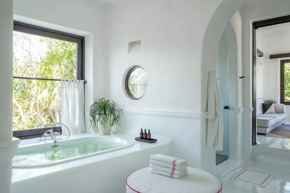 Bright bathroom with tub, arched doorway and stacked towels at Hotel Esencia.