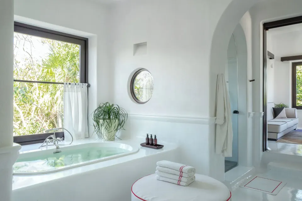 Bathtub set into a white alcove with porthole window and towels at Hotel Esencia.