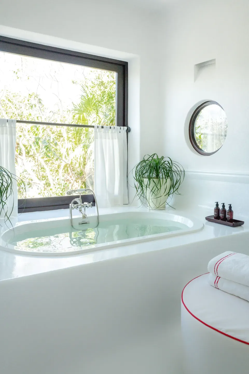 White soaking tub in The Esencia suite bathroom at Hotel Esencia with a garden view.