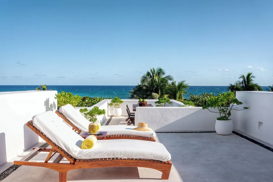 Sunlit terrace with two lounge chairs and ocean view at The Esencia suite, Hotel Esencia.