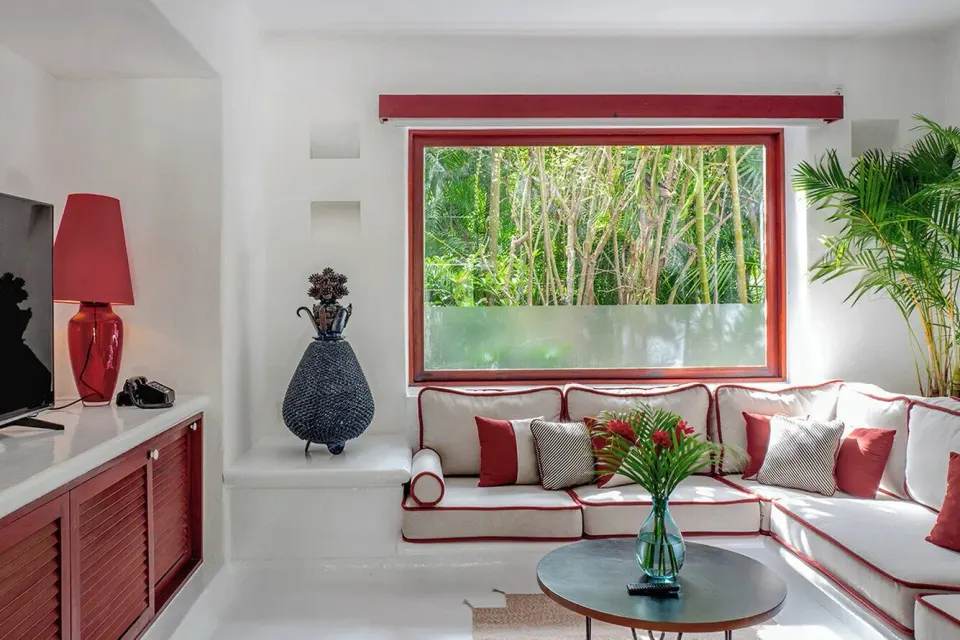 Corner seating with red-trimmed sofa and window jungle view at Hotel Esencia.