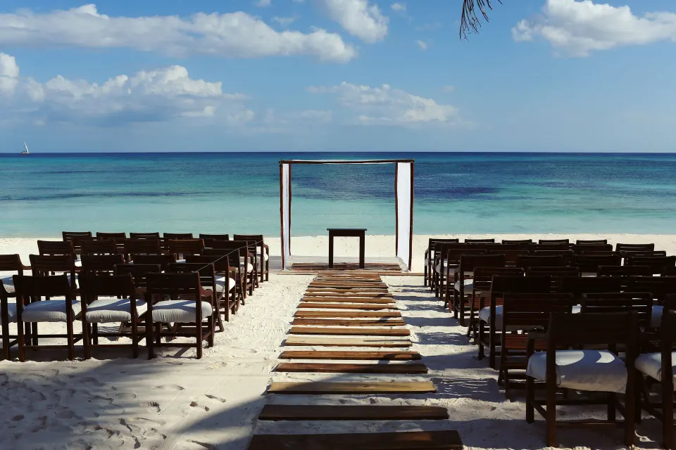 Wooden aisle and chairs set for a beach wedding on white sand at Hotel Esencia