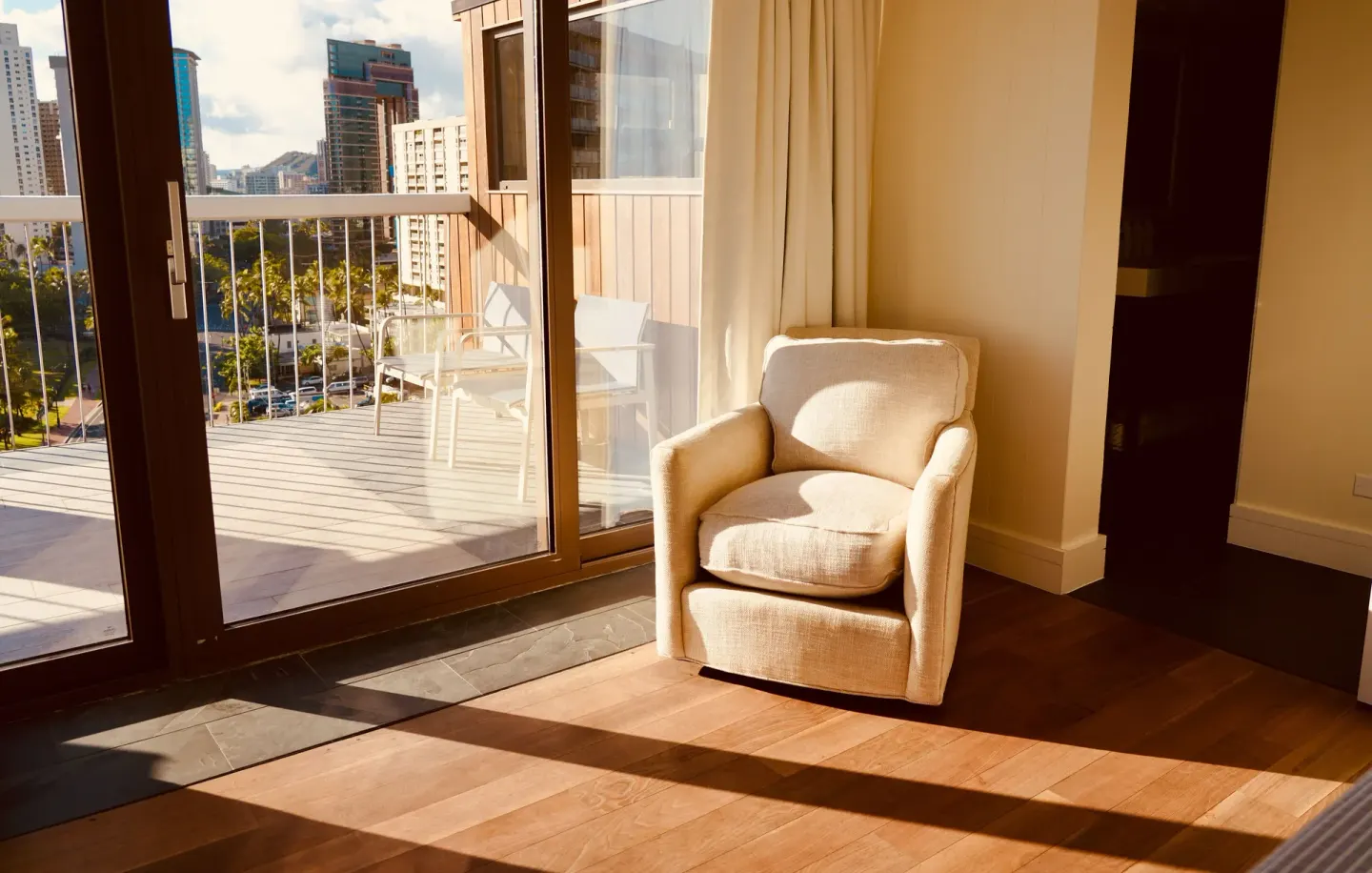 Sunlit guest room sitting area with balcony and city view at Hotel La Croix.