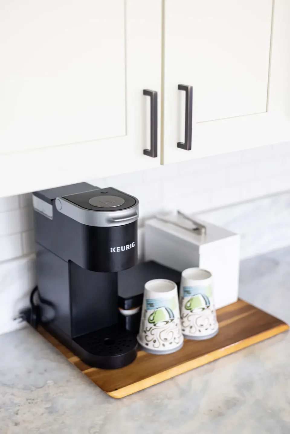 Guest room coffee maker and cups at Hotel La Croix set on a tray below white cabinets.