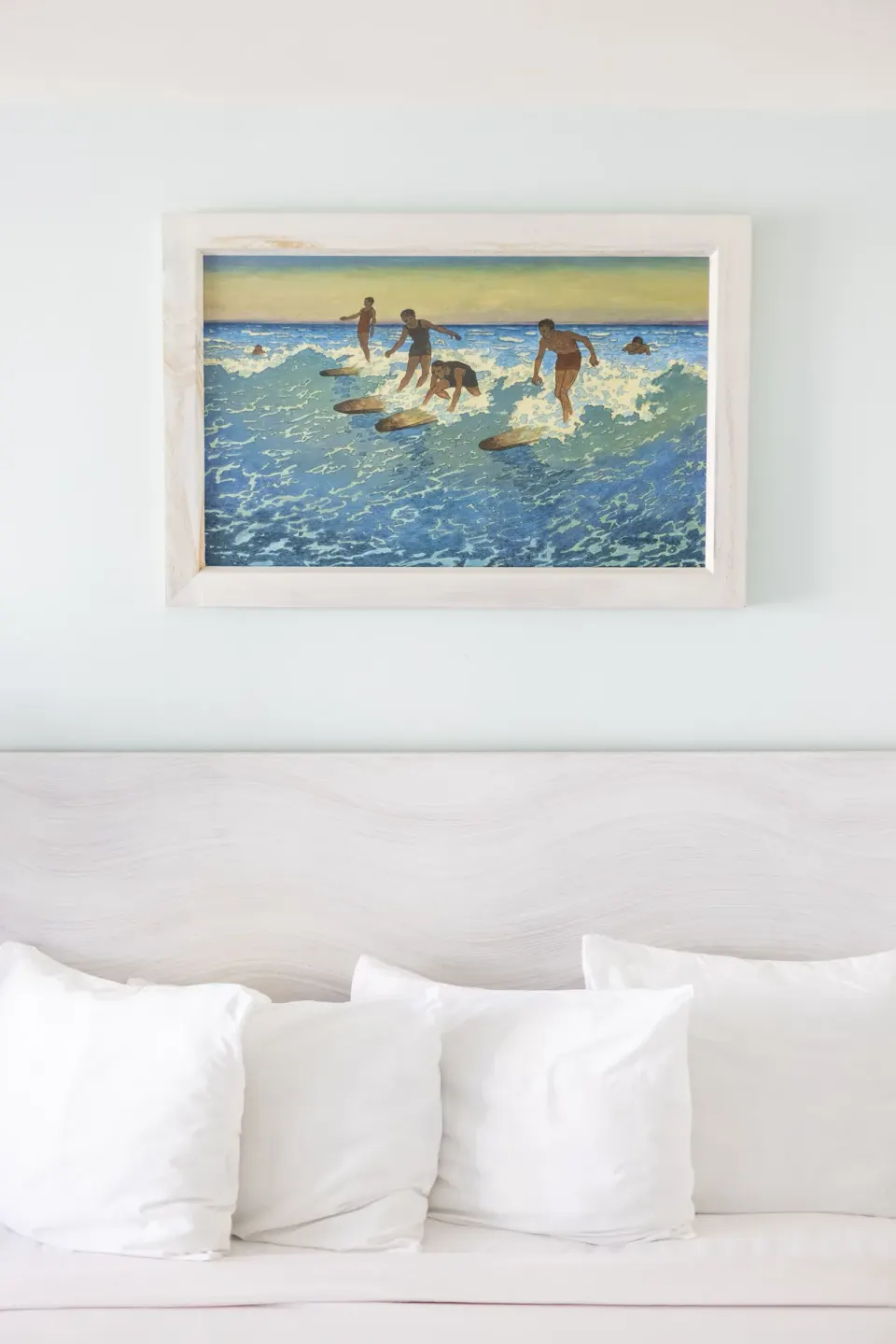 Framed surfer artwork above a white guest room bed at Hotel La Croix.