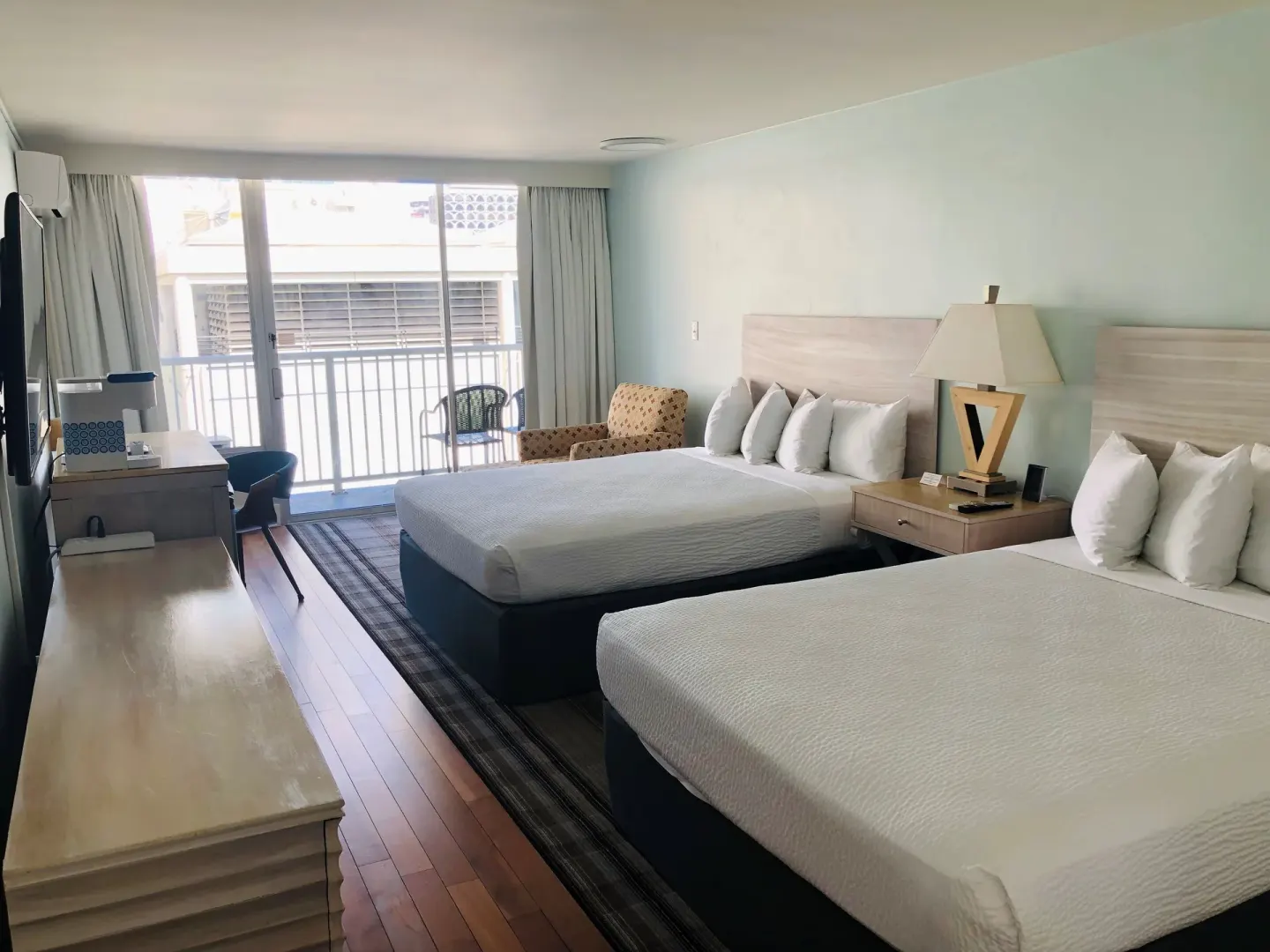 Guest room with two beds, desk, chair, and balcony doors at Hotel La Croix.