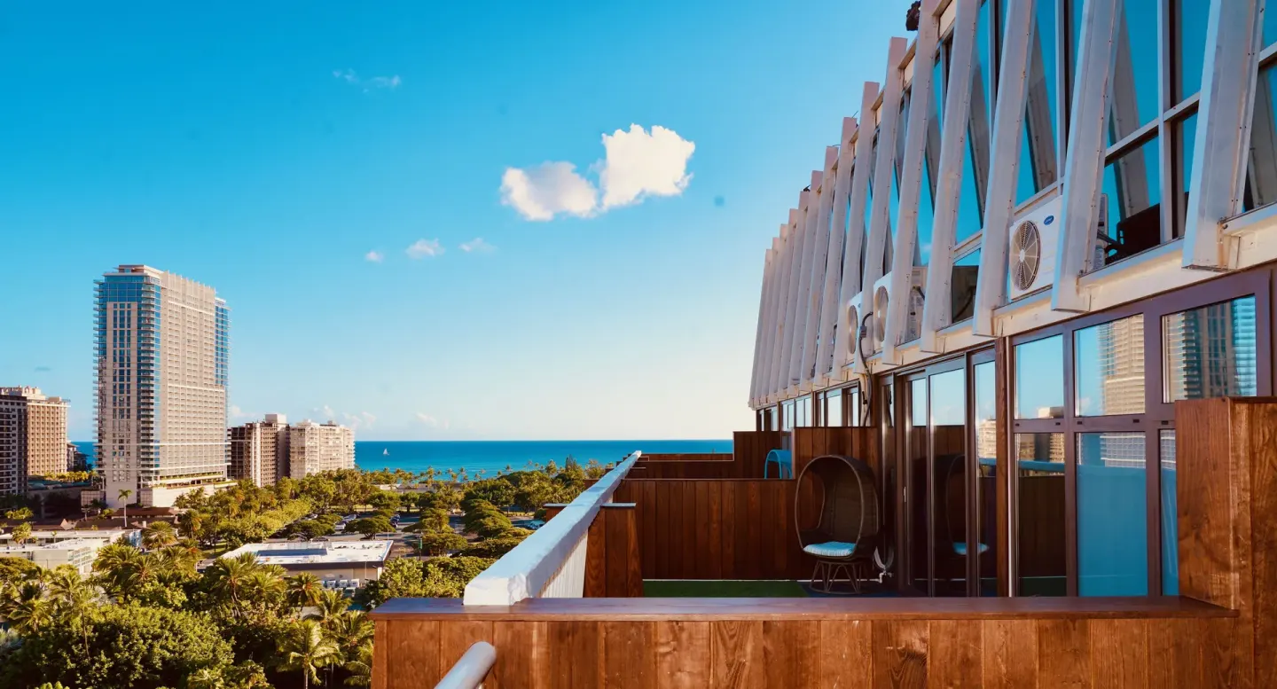 Rooftop terrace view from Hotel La Croix with city buildings, palms, and ocean beyond.