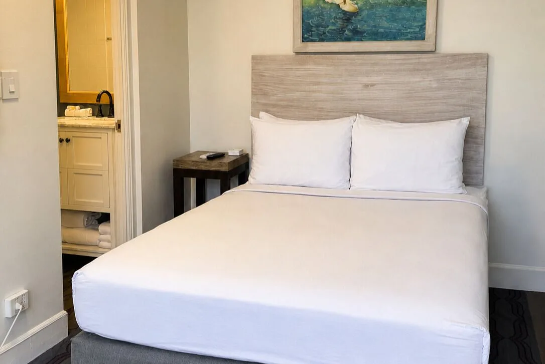 Bronze Room bed with wood headboard and bathroom vanity doorway at Hotel La Croix.