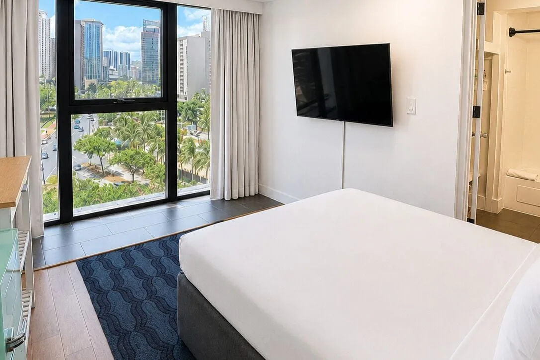 Bronze Room bed, wall-mounted TV, and tall city-view window at Hotel La Croix.