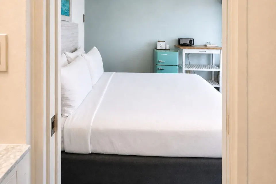 Bronze Room bed viewed from the bathroom doorway with mini fridge at Hotel La Croix.