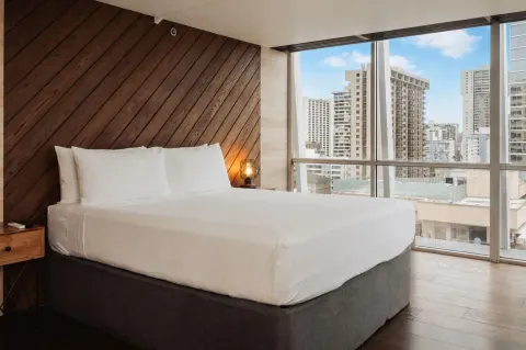 King bed by floor-to-ceiling city windows in Penthouse Hoku at Hotel La Croix.