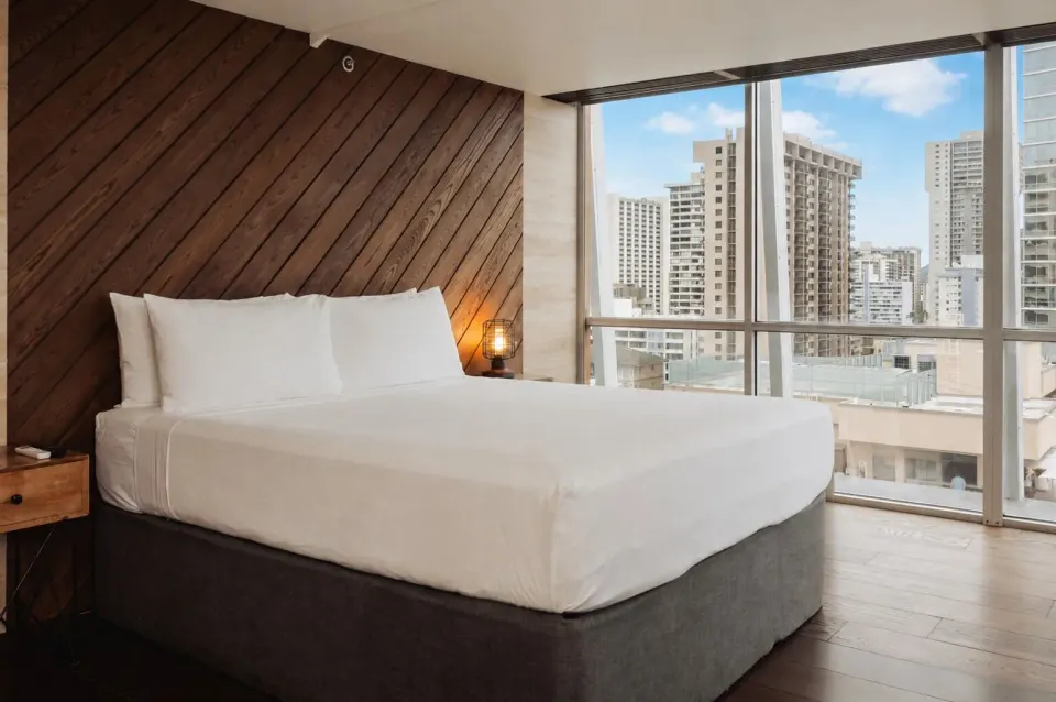 King bed by floor-to-ceiling city windows in Penthouse Hoku at Hotel La Croix.