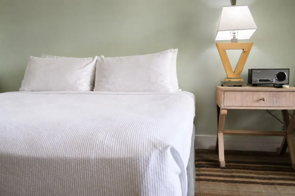 King bed with bedside lamp in a Premium Kalakaua Haus Corner Two Lanai room at Hotel La Croix.