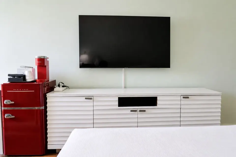 Wall-mounted TV and red mini fridge in a Premium Kalakaua Haus Corner Two Lanai room at Hotel La Croix.
