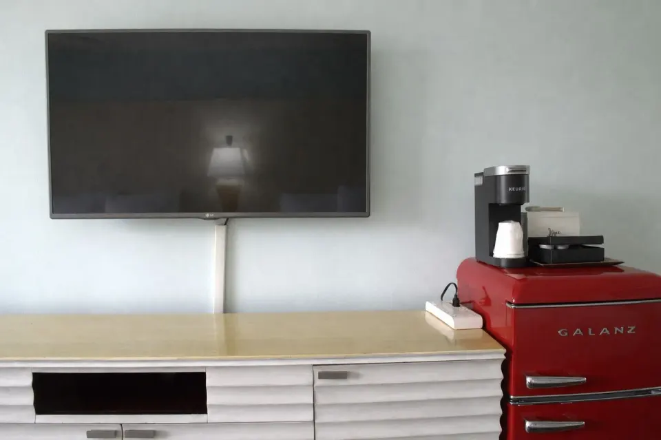 TV console, coffee maker, and red mini fridge in a Premium Kalakaua Haus room at Hotel La Croix.