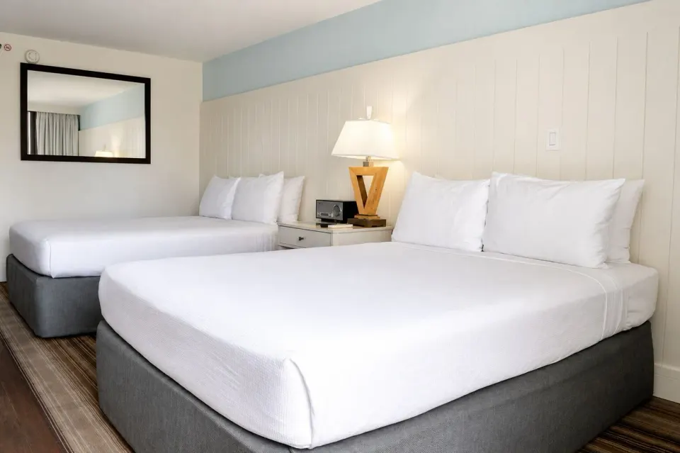Two white beds and bedside lamp in a Premium Kalakaua Haus room at Hotel La Croix.