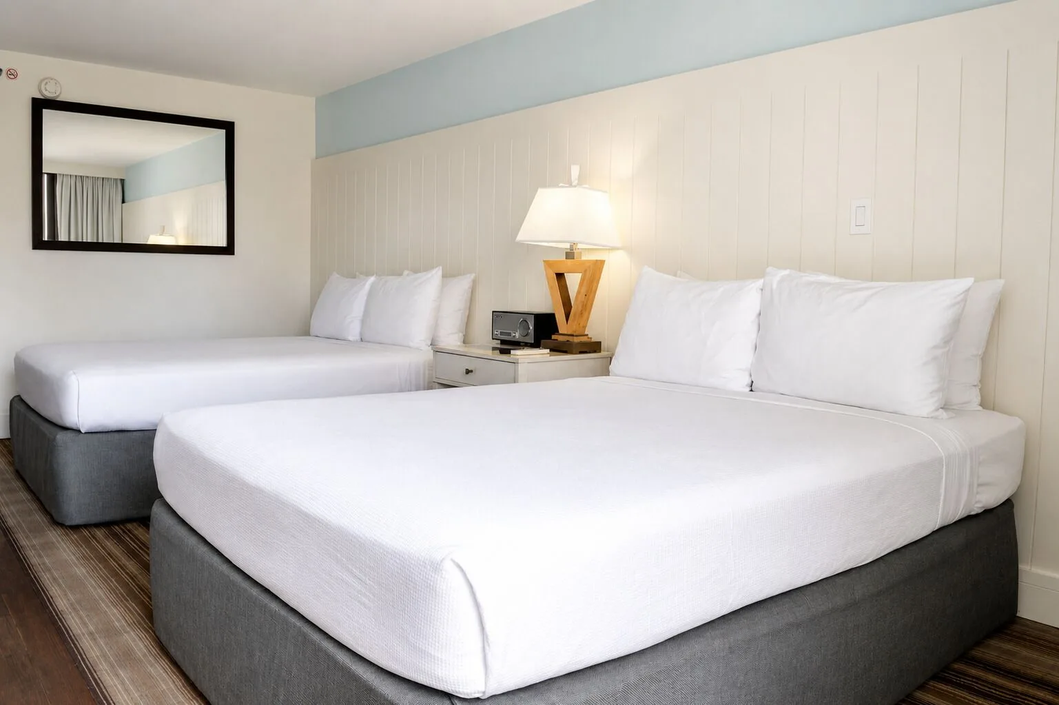 Two white beds and bedside lamp in a Premium Kalakaua Haus room at Hotel La Croix.