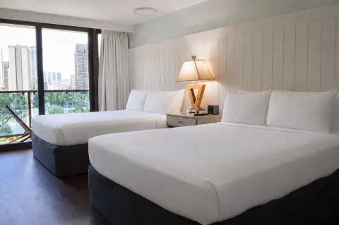 Two beds beside sliding balcony doors in a Premium Kalakaua Haus room at Hotel La Croix.