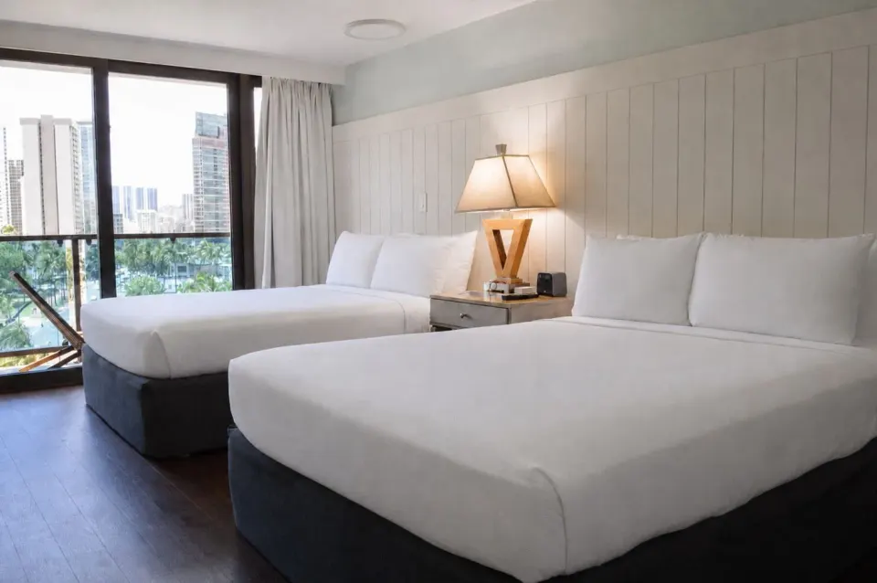 Two beds beside sliding balcony doors in a Premium Kalakaua Haus room at Hotel La Croix.