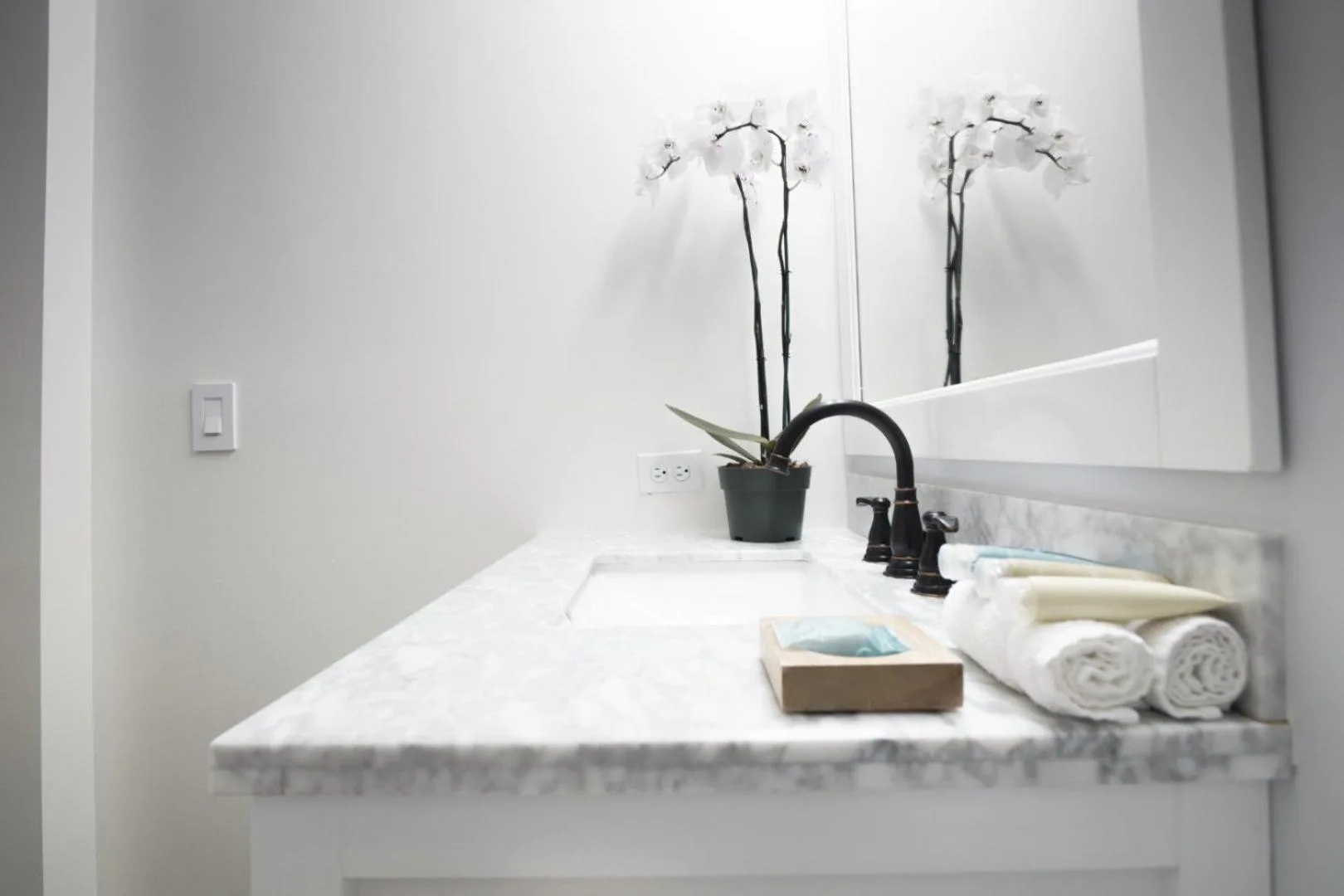 Bathroom vanity with marble counter, black faucet, towels, and orchid at Hotel La Croix.