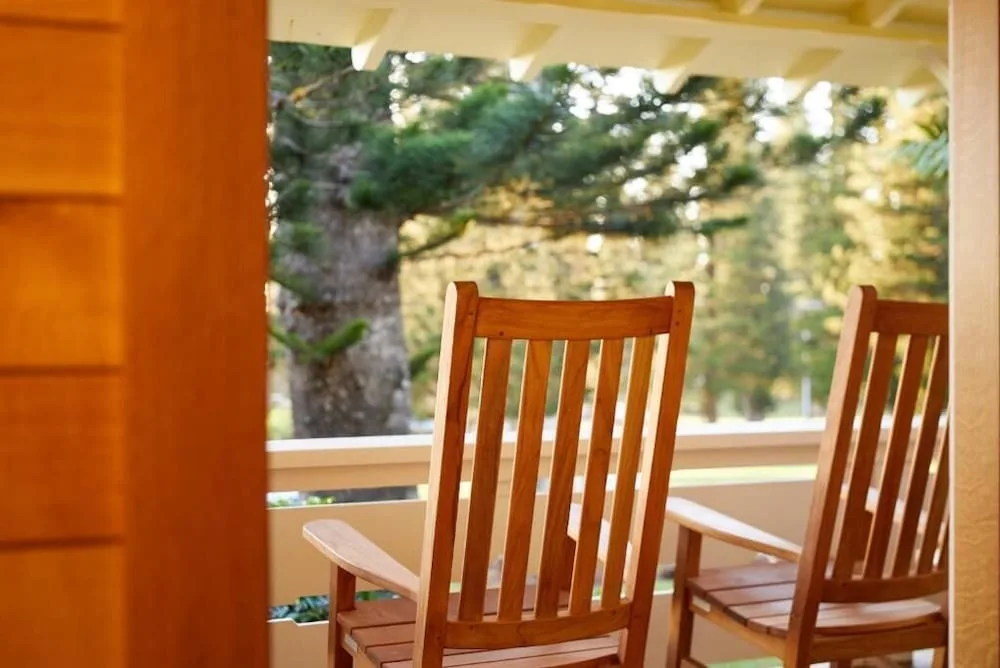 Covered porch at Hotel Lanai with two wooden chairs facing trees outside.