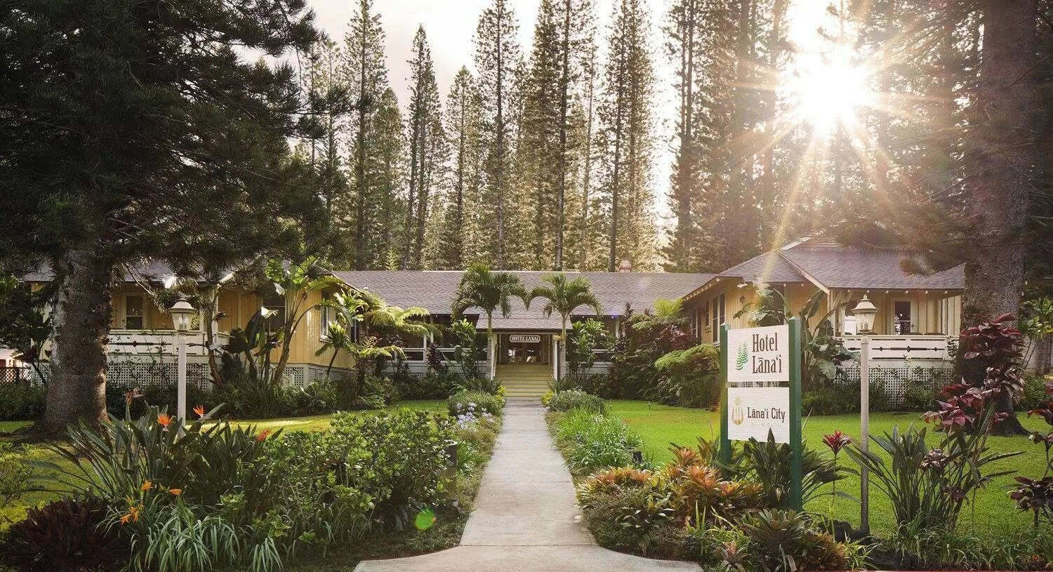 Garden walkway leading to the main entrance of Hotel Lanai with tall pines behind it.