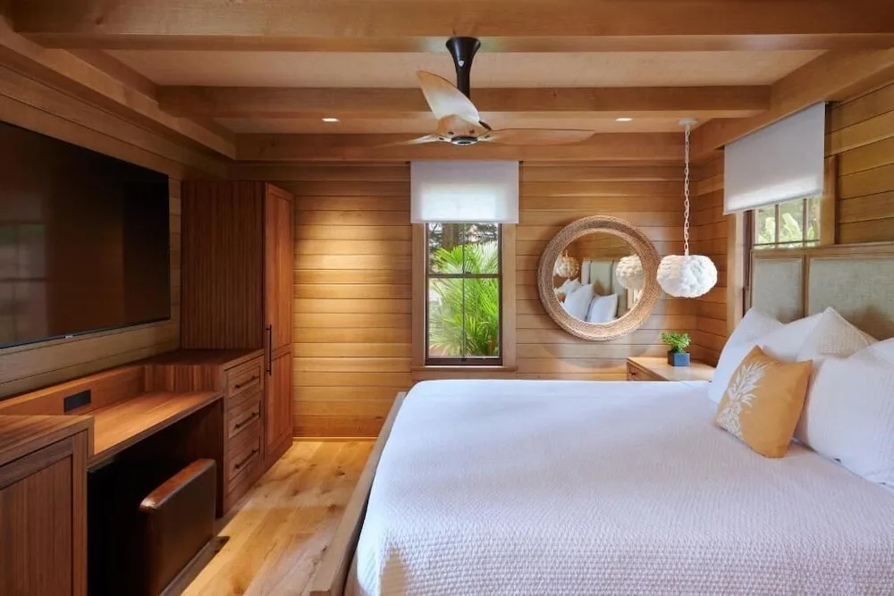 Guest room at Hotel Lanai with a king bed, wood walls, ceiling fan, desk, and TV.