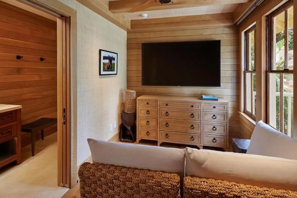 Guest room sitting area at Hotel Lanai with sofa, dresser, TV, and tall windows.