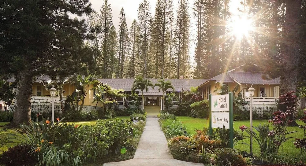 Sunlit exterior of Hotel Lanai with a garden path, sign, and tall trees.