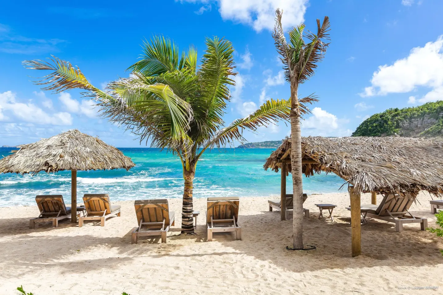 Beach loungers under thatched umbrellas by the sea at Hotel Manapany.