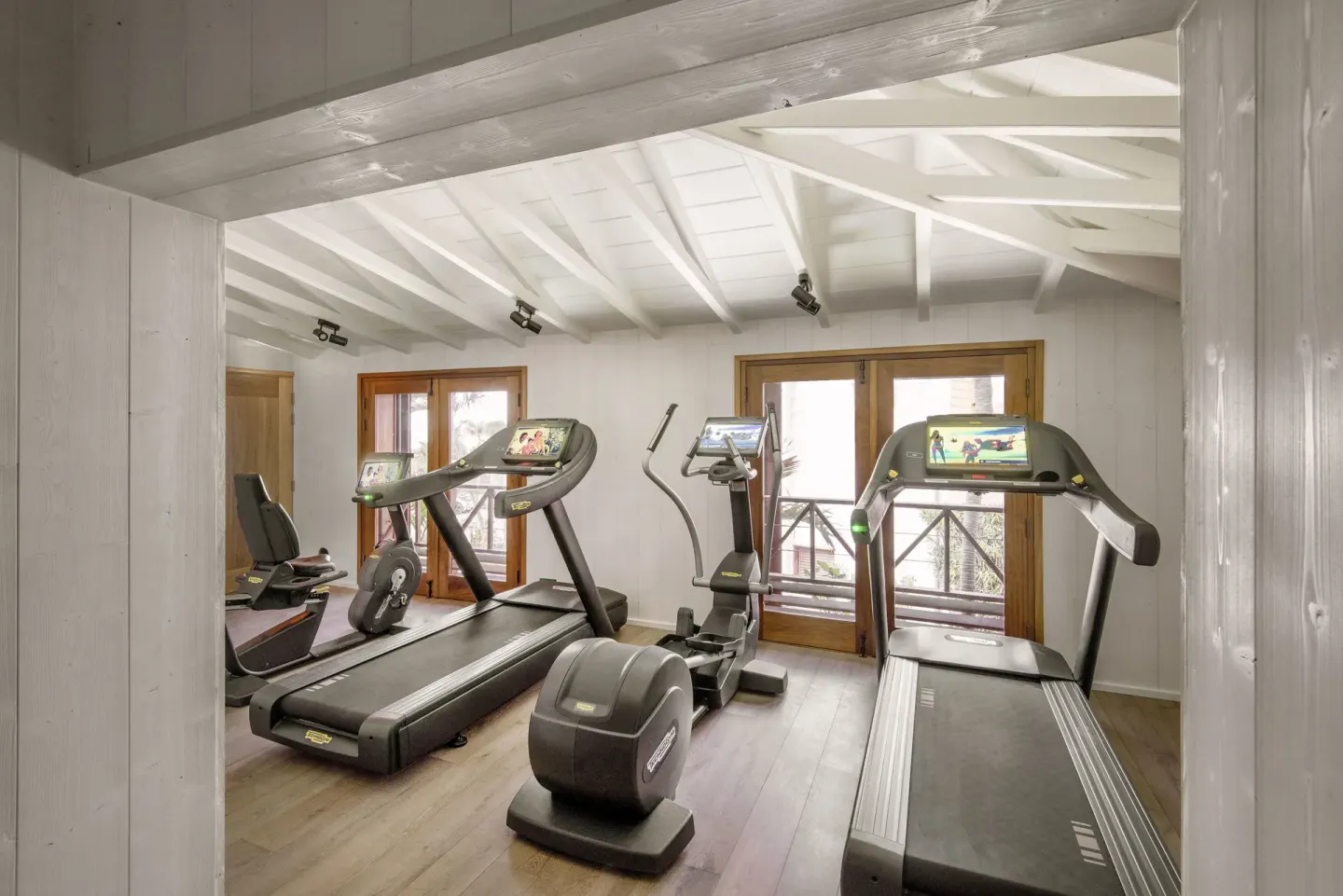 Fitness room with treadmills, cardio machines, and white timber walls at Hotel Manapany.